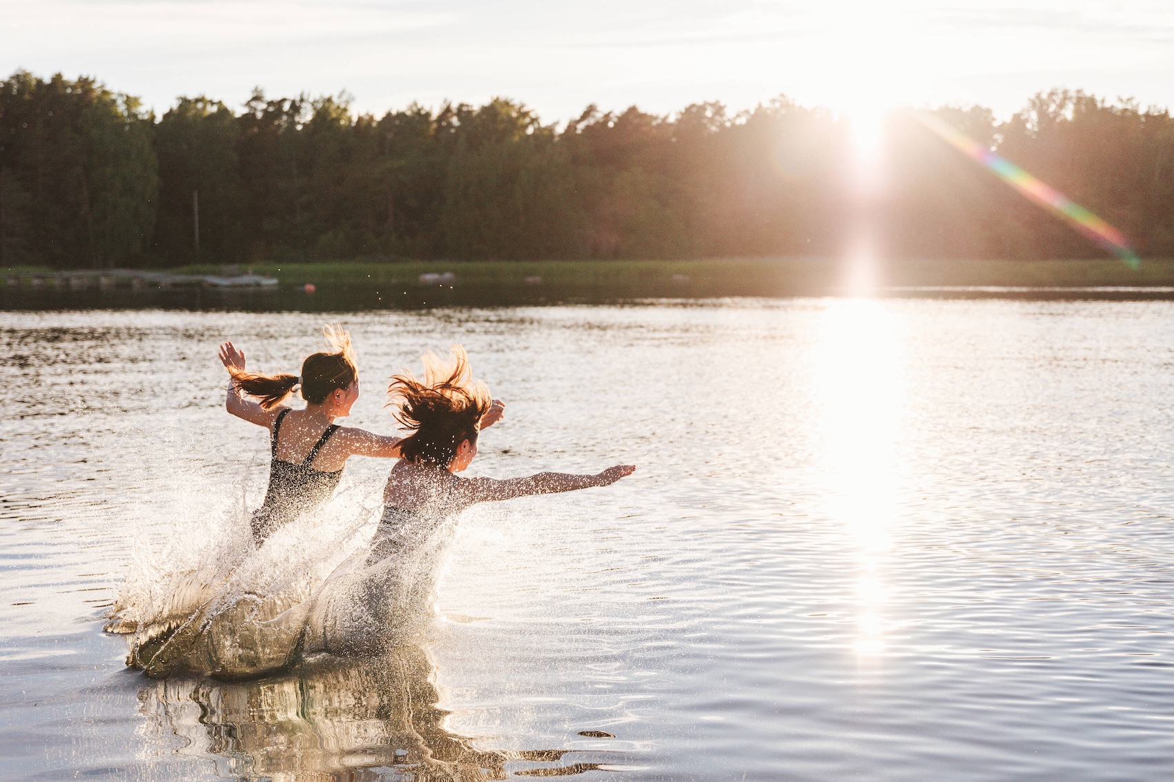 Two people running into a lake in the summer in Finland.